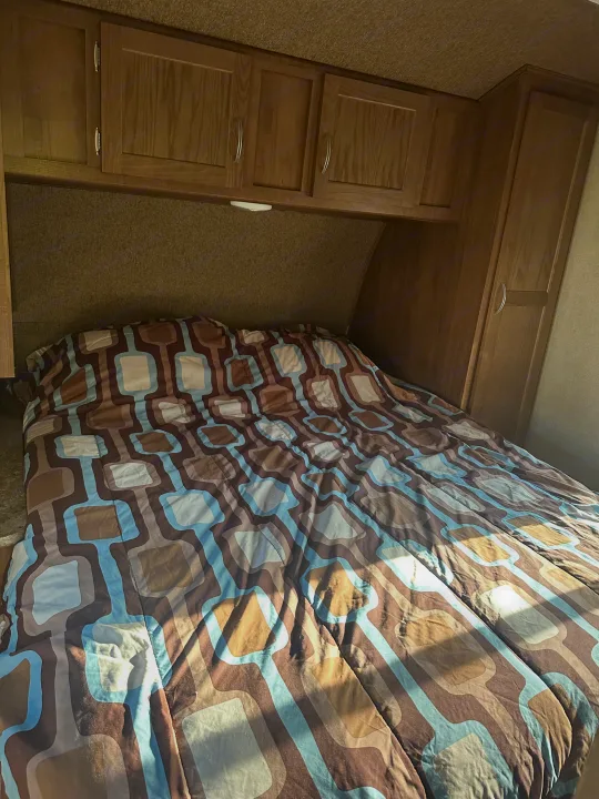 Cozy RV rental bedroom featuring a patterned comforter, overhead wood cabinets, and built-in wardrobe. Ideal for travel.. Gulf Stream Conquest 2017
