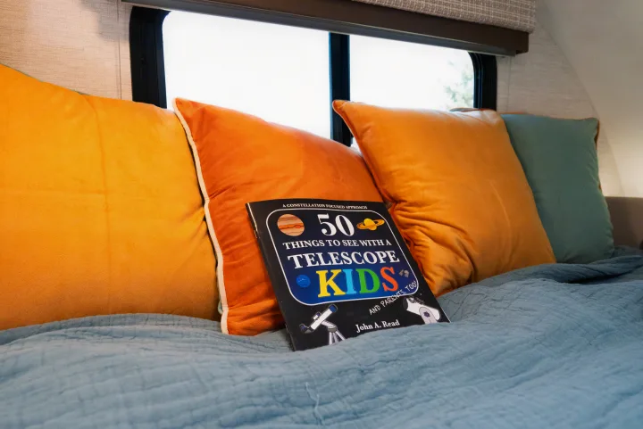 A kids' astronomy book, "50 Things to See with a Telescope," on an RV rental bed, ideal for starry nights.. Thor Motor Coach Eddie Bauer 21EBF 2025