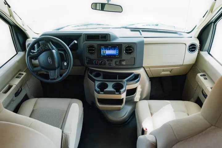 Interior view of a Ford E-Series RV rental cockpit, featuring the dashboard, steering wheel, infotainment, and front seats.. Thor Motor Coach Eddie Bauer 21EBF 2025