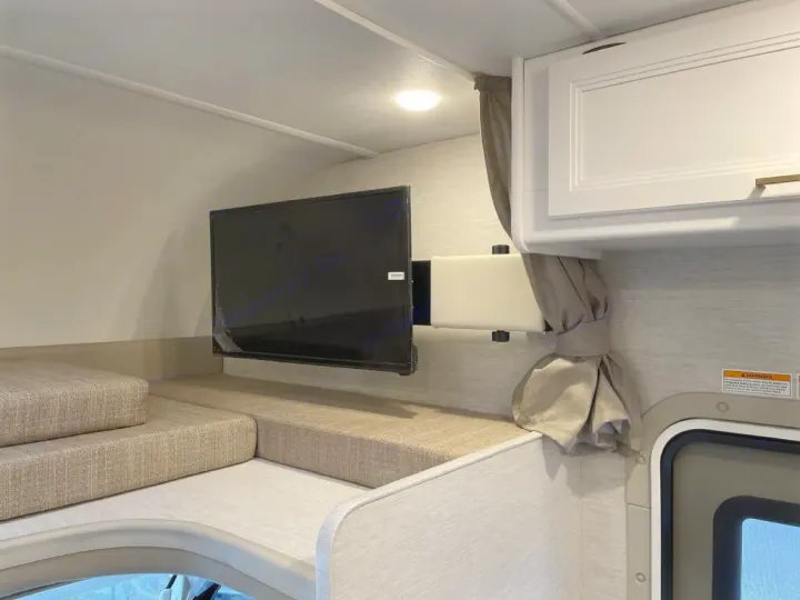Cozy RV rental interior featuring a wall-mounted TV, plush upholstered bed/bunk, and a white overhead storage cabinet.. Thor Motor Coach Eddie Bauer 21EBF 2025