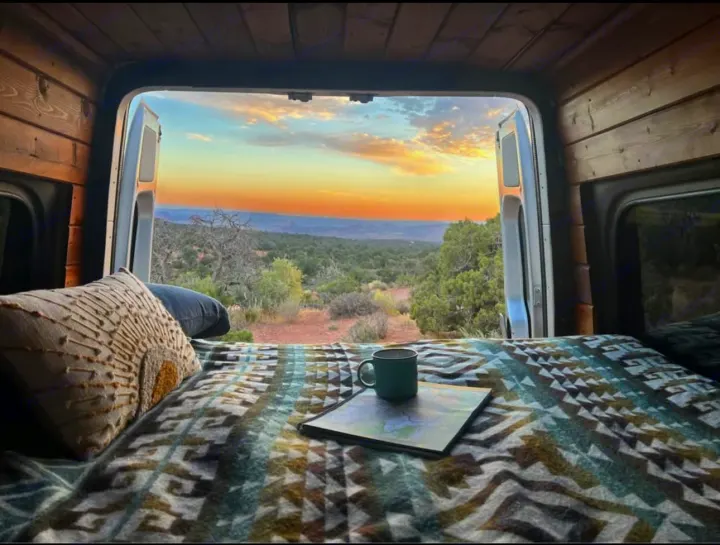 Scenic RV rental adventure: cozy bed setup with a stunning sunset over the landscape, seen from inside the van.. Mercedes Sprinter 2008