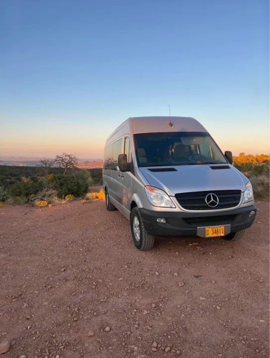 This silver Mercedes Sprinter RV rental camper van enjoys a stunning desert sunset from a dirt road.. Mercedes Sprinter 2008