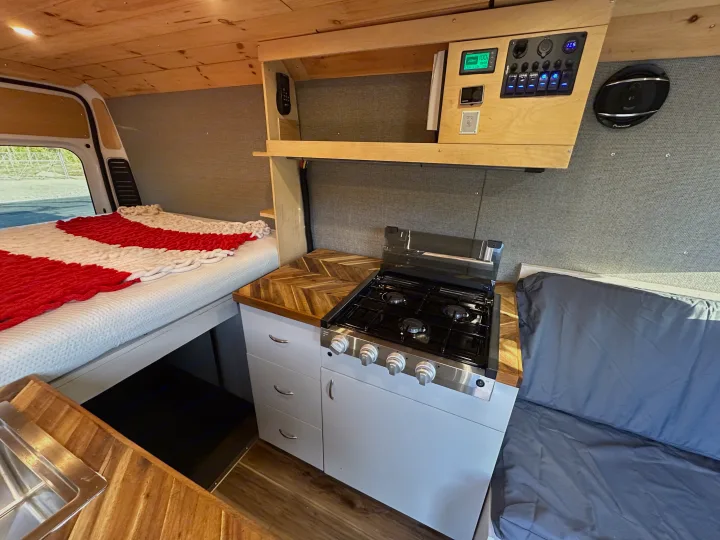 RV rental interior: This camper van features a bed, kitchen with stove and sink, wooden counters, and a control panel.. Dodge Promaster 3500 2020