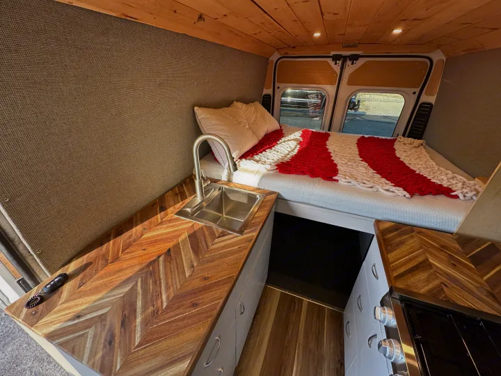 Cozy camper van interior for your next RV rental adventure, featuring a bed, kitchen, and wood finishes.. Dodge Promaster 3500 2020