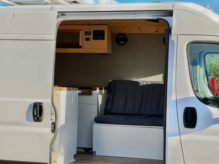 White camper van RV rental interior: custom control panel, kitchenette, and bench seating visible through open side door.. Dodge Promaster 3500 2020