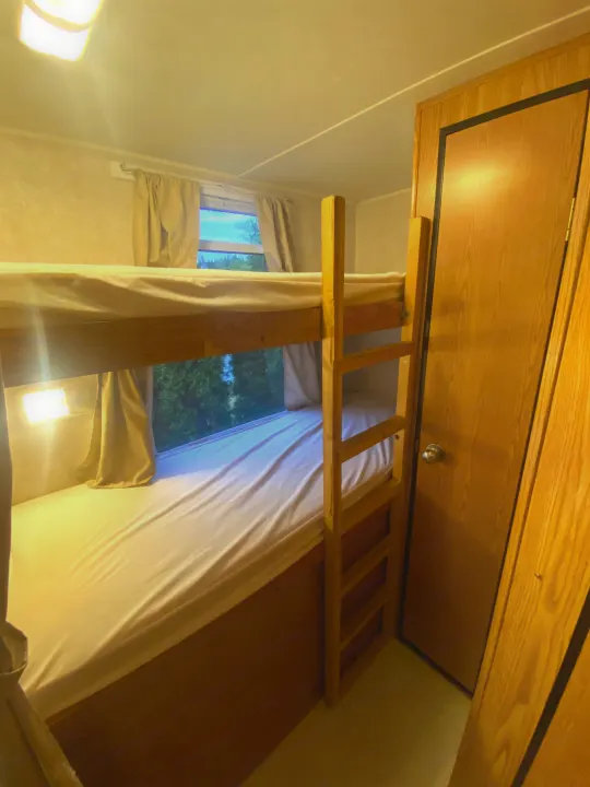 Cozy bunk beds in an RV rental, featuring a view of trees outside and warm lighting, perfect for compact travel accommodation.. Dutchmen Express 2001