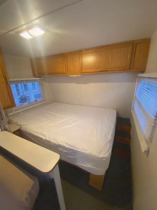 This RV rental's bedroom offers a cozy white bed, wooden overhead cabinets, and natural light from side windows.. Dutchmen Express 2001