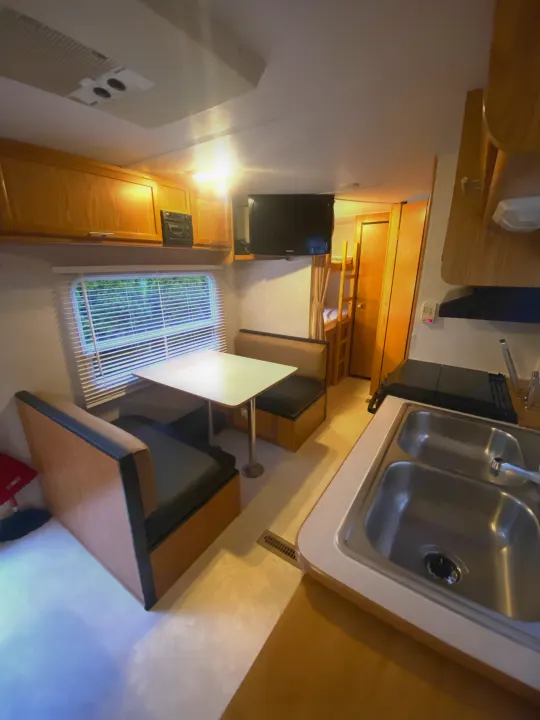 Cozy RV rental interior showcasing kitchen sink, dining booth, mounted TV, and bunk beds.. Dutchmen Express 2001