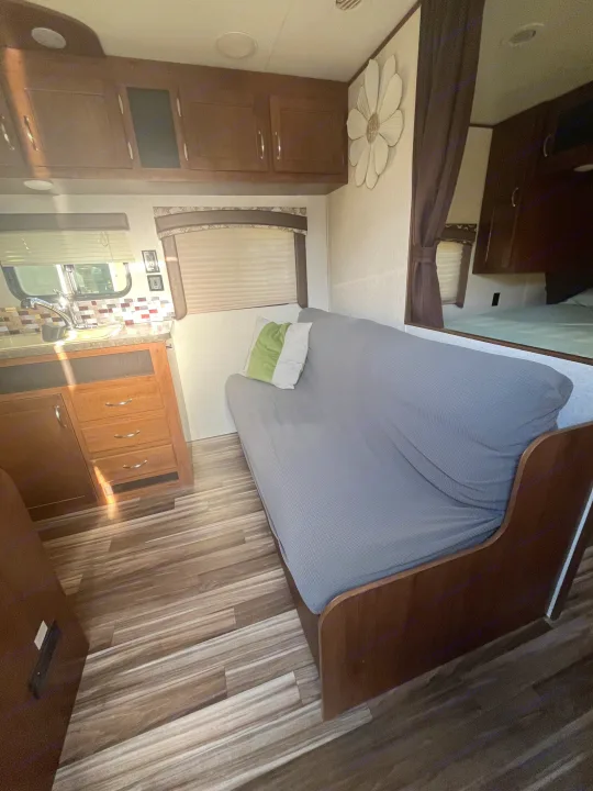 RV rental interior features a grey couch, wood cabinets & flooring, kitchen, and bedroom access for a comfortable trip.. Jayco Jaycoflight 2017
