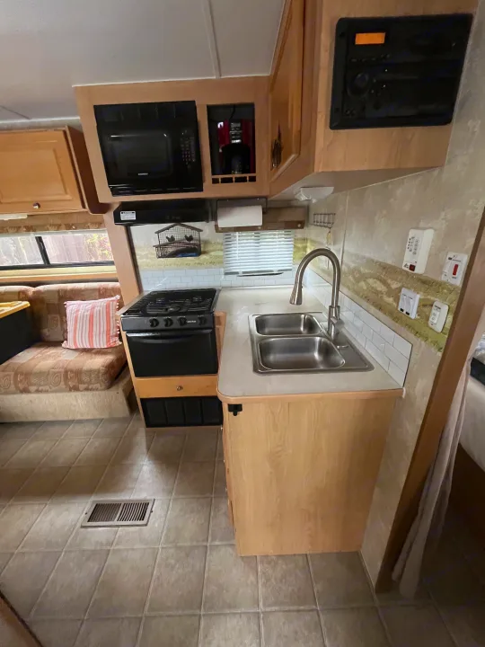 Cozy RV rental interior featuring a full kitchen with stove, microwave, sink, and comfortable bench seating.. Thor Motor Coach Wave 2007