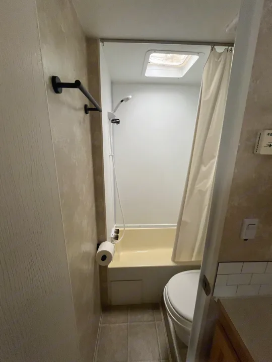 This RV rental bathroom features a compact shower/tub, toilet, and towel bar, designed for travel convenience.. Thor Motor Coach Wave 2007