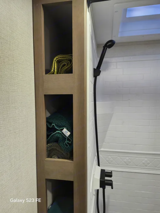 RV rental bathroom: textured walls, built-in towel storage, white subway tile shower with black fixtures, and a skylight.. Grand Design Transcend 2025