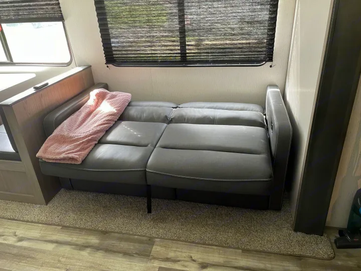 A cozy gray sofa/futon with a pink blanket inside an RV rental, offering a comfortable spot for your travel adventures.. Coleman Lantern 2022