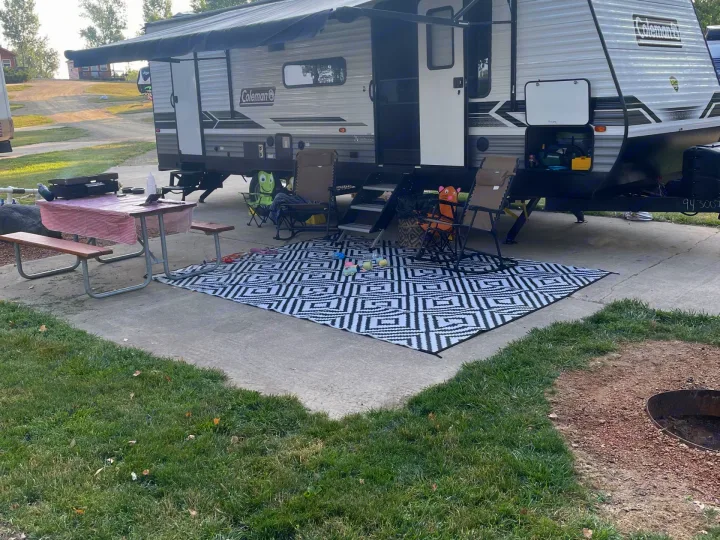 Relaxing at a campsite with an RV rental, featuring an outdoor mat, picnic table, and chairs for cozy outdoor living.. Coleman Lantern 2022