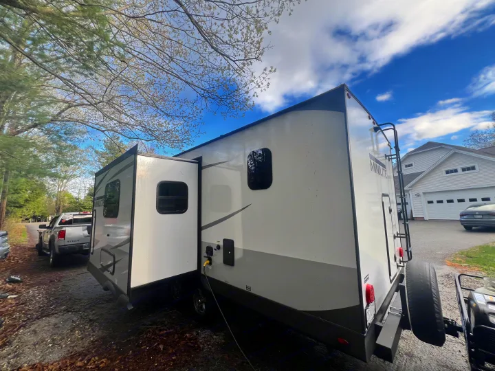 This RV rental is a white and gray travel trailer, fully set up outdoors with its slide-out extended and power connected.. Forest River Rockwood Mini Lite 2023