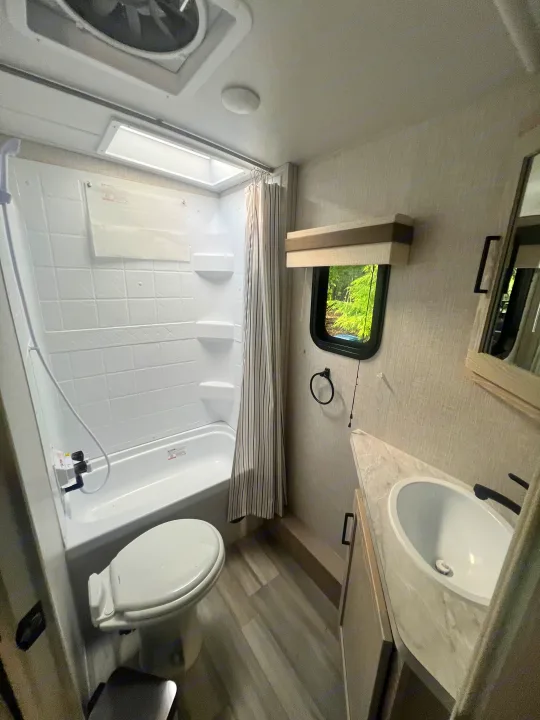 This RV rental bathroom provides essential amenities: a functional shower/tub, compact toilet, and practical sink vanity.. Forest River Rockwood Mini Lite 2023