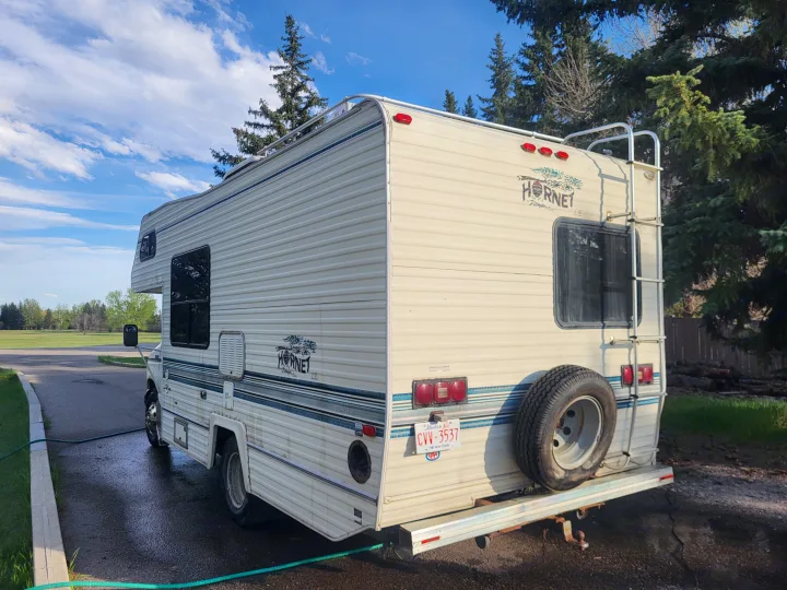 White Hornet RV rental, seen from the rear with a spare tire and ladder, parked on a paved drive, ideal for travel.. Ford Econoline 1992