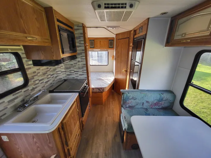 Spacious rv rental interior features a full kitchen, dining booth, and cozy bedroom. Modern flooring & backsplash seen.. Ford Econoline 1992