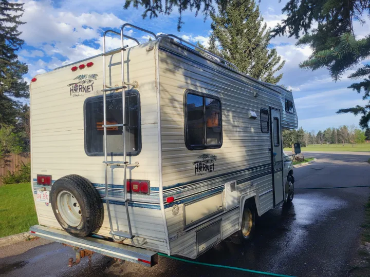 This white and blue Hornet motorhome, suitable for an rv rental, is parked on a wet drive after a wash.. Ford Econoline 1992