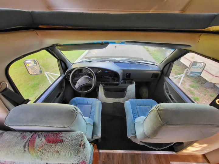 RV rental interior: Looking from the rear into the driver's cab, showing dashboard, front seats, and an overhead sleeping area.. Ford Econoline 1992