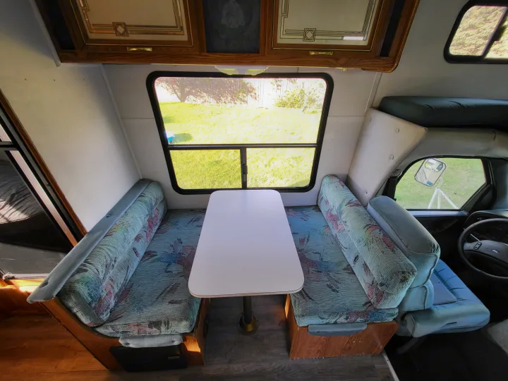 Interior of an RV rental showing a bright dinette with patterned benches, overhead cabinets, and large windows.. Ford Econoline 1992