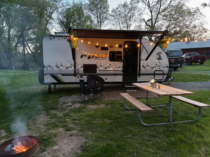 Cozy RV rental campsite with R-Pod, picnic table, string lights, and fire pit under trees.. Forest River R-Pod 2022