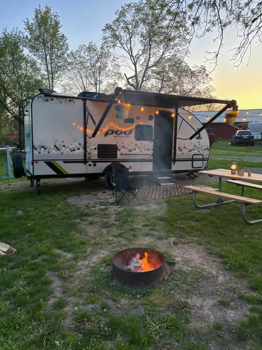 Enjoying a cozy RV rental campsite with a warm campfire, string lights, and picnic table at twilight.. Forest River R-Pod 2022