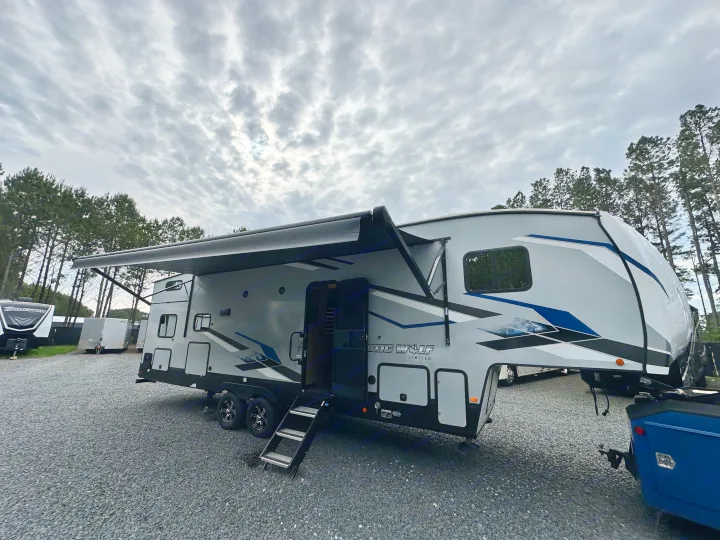 Large, modern Arctic Wolf fifth-wheel rv rental with extended awning & steps on gravel, ready for adventure under cloudy skies.. Forest River Cherokee Arctic Wolf 2022