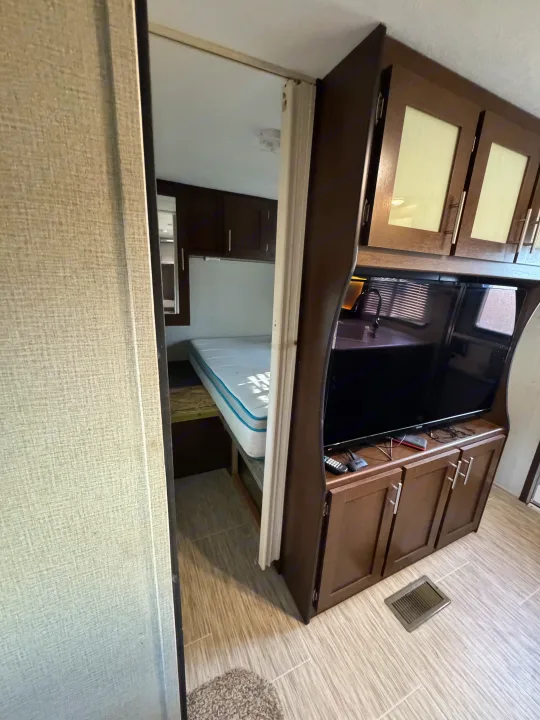 This RV rental interior highlights a bunk bed area and living space with a TV, kitchen sink, and storage.. Forest River Avenger ATI 2018
