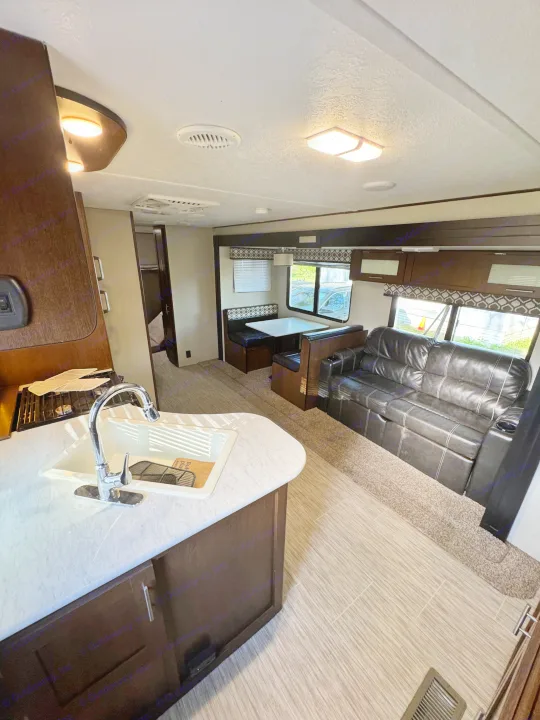 Spacious RV rental interior: kitchen with sink, dining booth, and dark leather sofa. Enjoy comfortable travel living.. Forest River Avenger ATI 2018