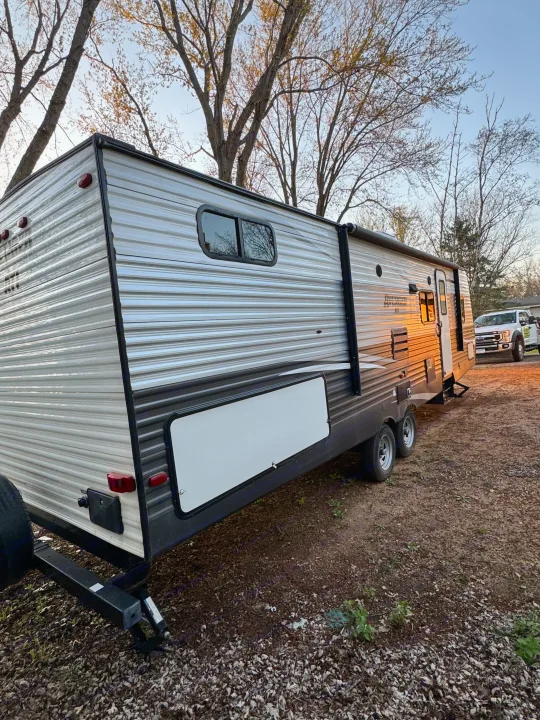 Sunlit travel trailer, an ideal RV rental for outdoor adventures, parked with a truck and trees in the background.. Forest River Avenger ATI 2018