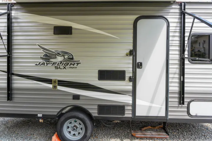 Jayco Jay Flight SLX RV rental, parked on gravel. Close-up of the exterior, showing door, window, vents, and utility connections.. Jayco Jay Flight 2021
