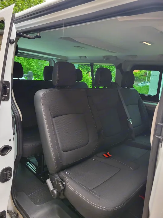 Inside this RV rental: a spacious passenger van interior with three rows of black seats, ready for comfortable group trips.. Renault Trafic 2025
