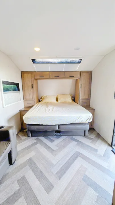 RV rental bedroom features a comfy bed with yellow linens, surrounded by wood cabinets, and a modern herringbone floor.. Ember Overland 2023