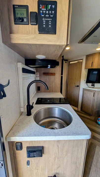 RV rental interior showcasing a modern kitchenette with a sink, cooktop, and advanced control panels.. Ember Overland 2023