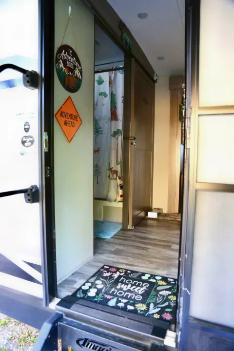 Explore this cozy RV rental interior: "Home sweet home" welcome mat, "Adventure" signs, and nature-themed shower.. Grand Design Imagine 2020