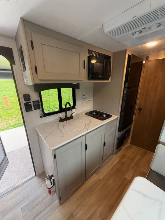 Inside this rv rental: a compact kitchen with white marble-look counter, sink, stovetop, microwave, and light wood cabinets.. Coachmen Clipper 17CBH 2025