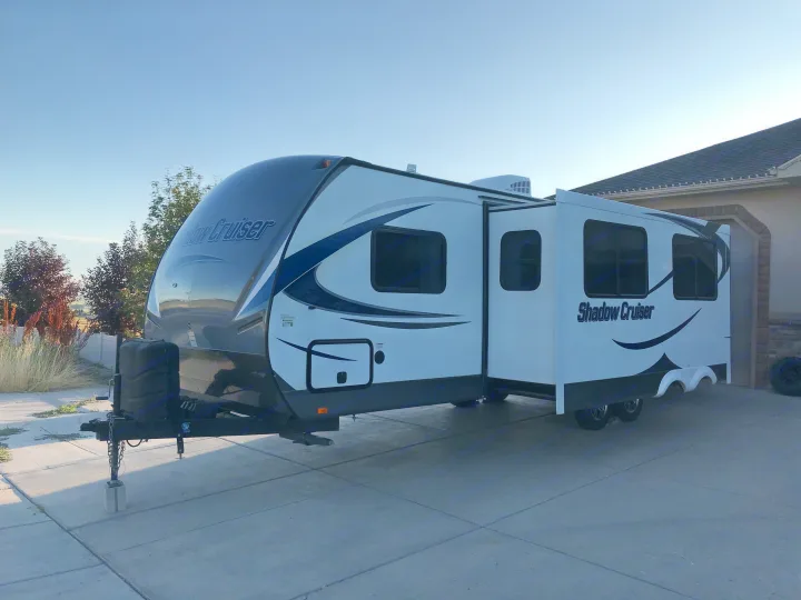 White and gray Shadow Cruiser travel trailer, an RV rental, parked with slide-out extended on a concrete driveway.. Cruiser RV Shadow Cruiser 2015
