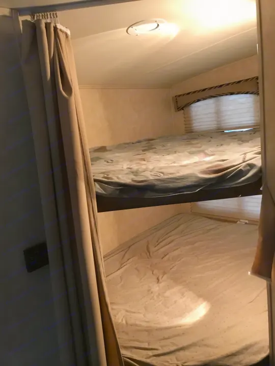 Inside an RV rental: neatly made bunk beds with light bedding, a window with blinds, and a bright ceiling light.. Cruiser RV Shadow Cruiser 2015