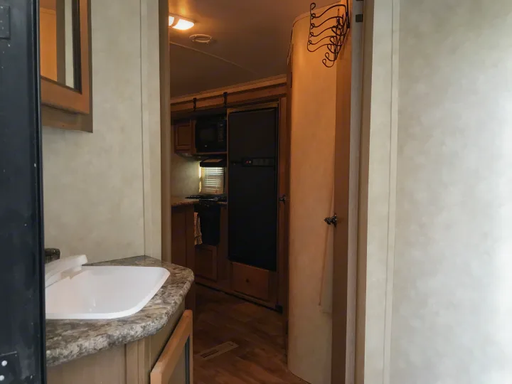 An RV rental's practical interior showing kitchen with microwave, stove, fridge, and a sink area on a speckled countertop.. Cruiser RV Shadow Cruiser 2015