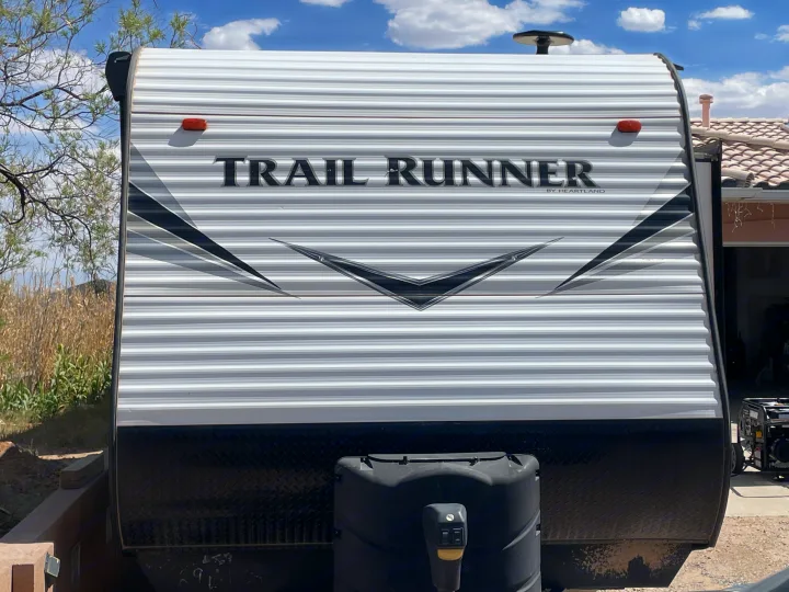 Front view of a white Trail Runner RV, showing its corrugated siding, propane tank, and black diamond plate. Perfect for rv rental.. Heartland RVs Trail Runner 2019