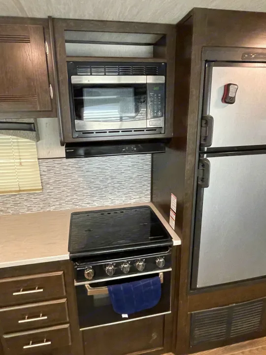 Compact kitchen in an RV rental, featuring a microwave, range, and refrigerator. Includes modern backsplash and ample cabinets.. Heartland RVs Trail Runner 2019