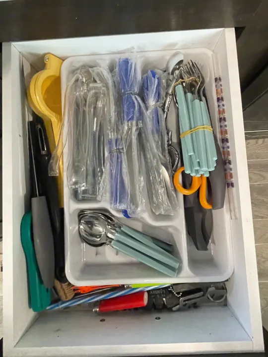 RV rental kitchen drawer fully stocked with utensils, new cutlery in plastic, yellow juicer, and other kitchen tools.. Heartland RVs Trail Runner 2019