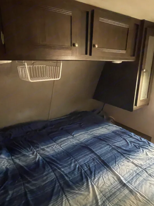 Cozy RV rental bedroom with dark wood cabinets, a blue striped bed, and a wall-mounted TV. Compact and functional.. Heartland RVs Trail Runner 2019