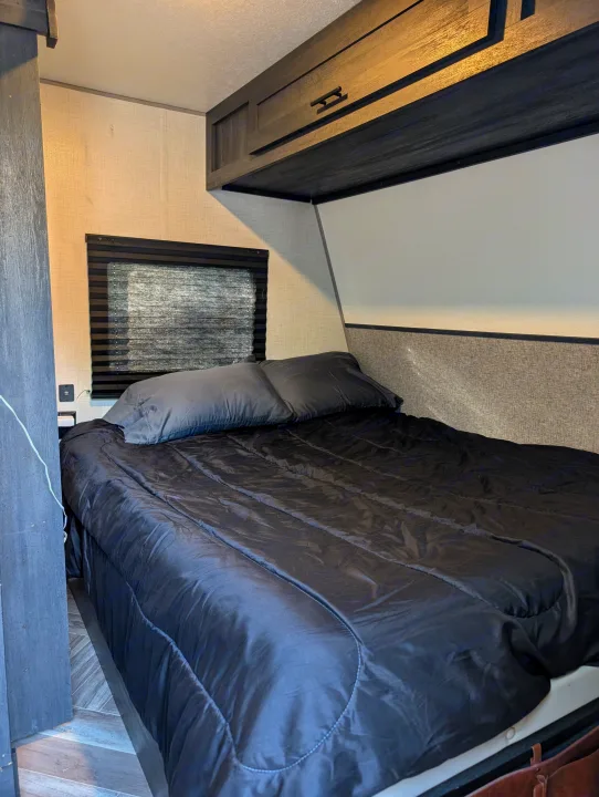 Cozy RV rental bedroom with a dark bed, window blinds, & overhead cabinets for comfortable travels.. Forest River 2700TH 2021