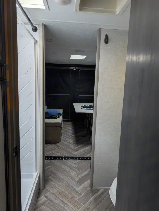 Inside an RV rental: Shower, herringbone flooring, and a multi-purpose living/garage area with a table and seating.. Forest River 2700TH 2021