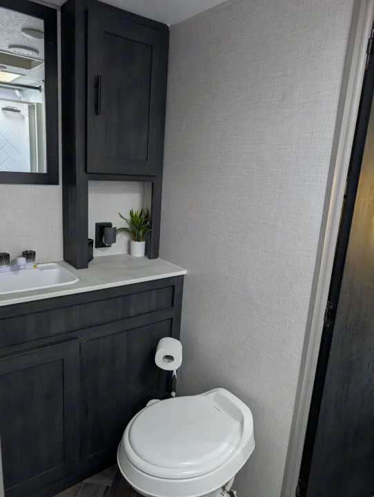 RV rental bathroom with dark wood vanity, white sink, toilet, and mirror, designed for comfortable, compact travel.. Forest River 2700TH 2021