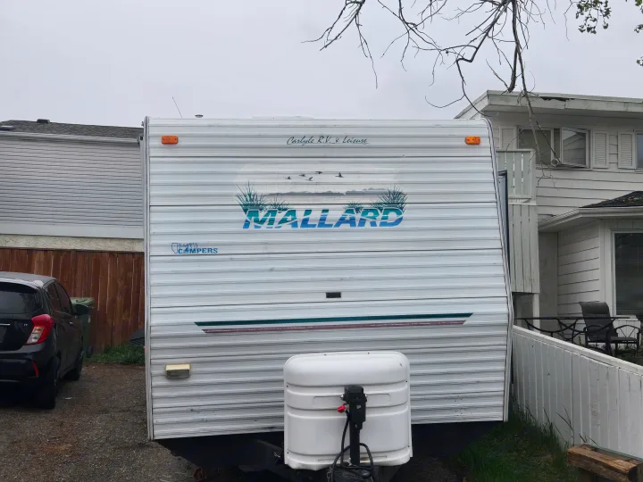 Front view of a white Mallard RV, a potential rv rental, parked outdoors. Features include a propane tank and a "Happy Campers" sticker.. Fleetwood Mallard 2004