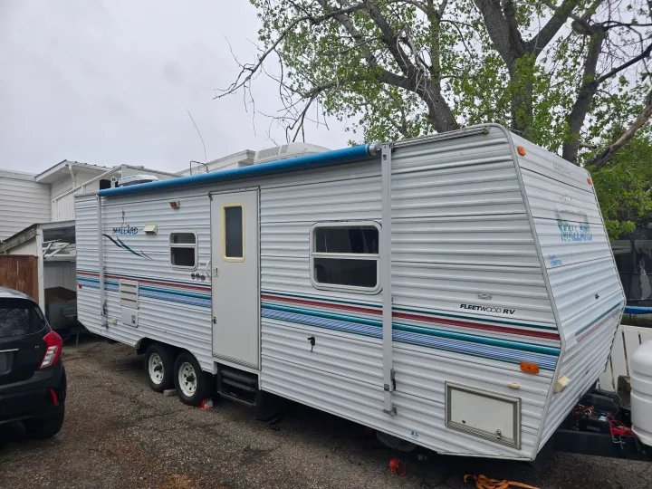 A white Fleetwood Mallard travel trailer with a blue awning, parked outdoors, is an excellent RV rental option.. Fleetwood Mallard 2004