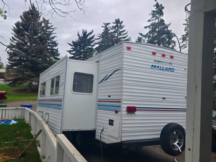 A white Fleetwood Mallard RV rental, a travel trailer with an extended slide-out, parked outdoors.. Fleetwood Mallard 2004